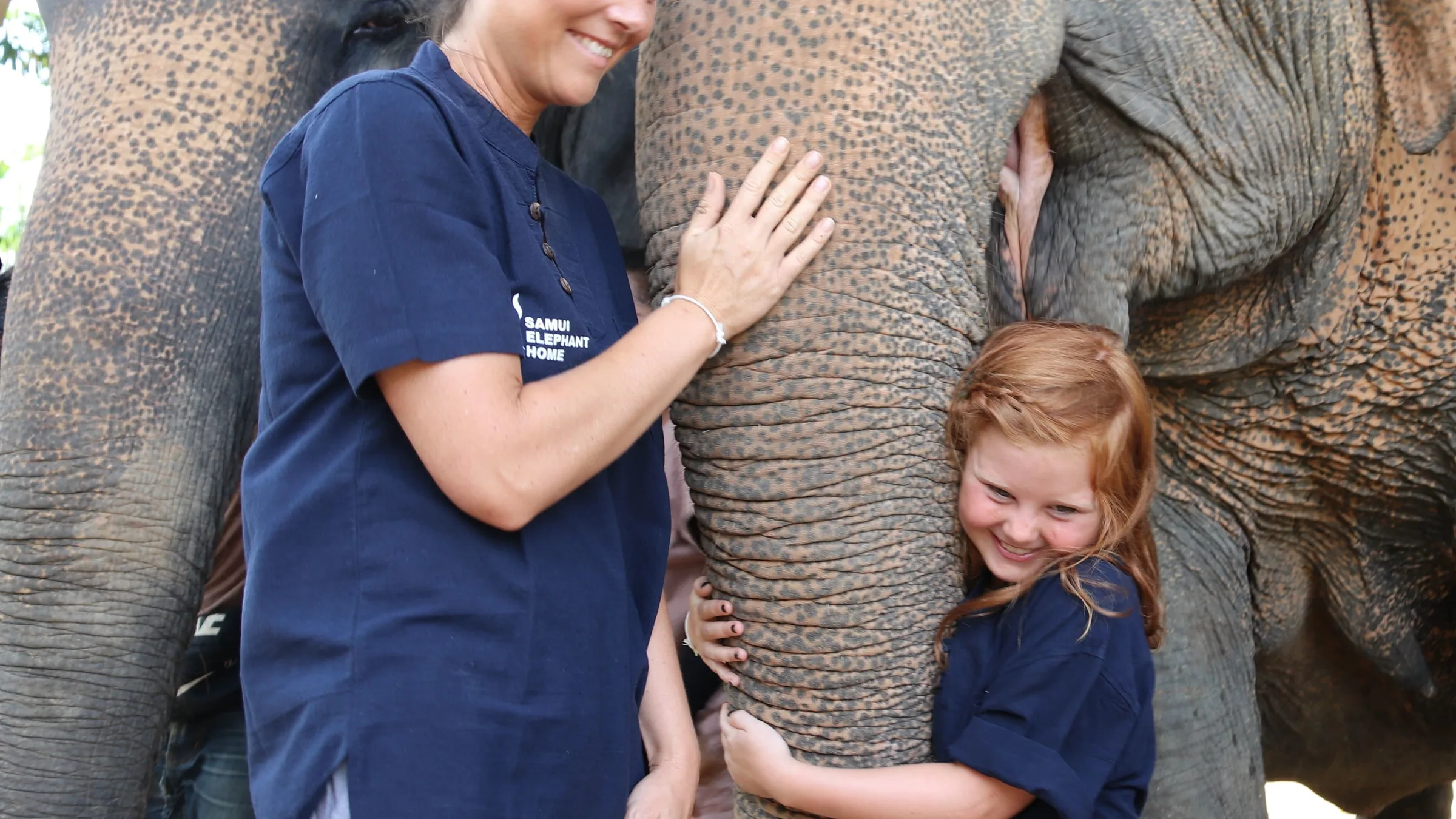 A mother and child beside an elephant at Samui Elephant Home