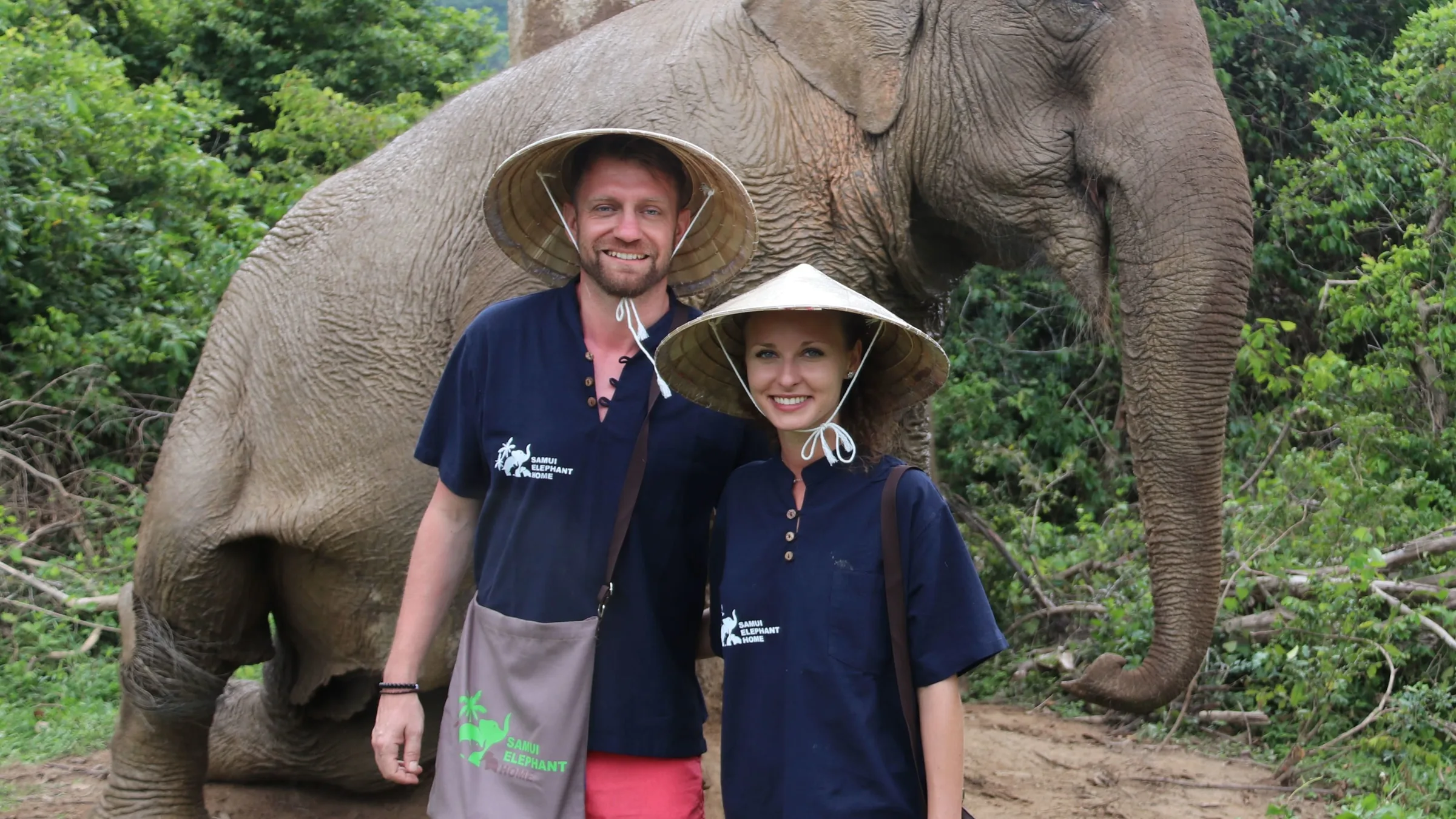 Visitors beside an elephant in the grounds of Samui Elephant Home
